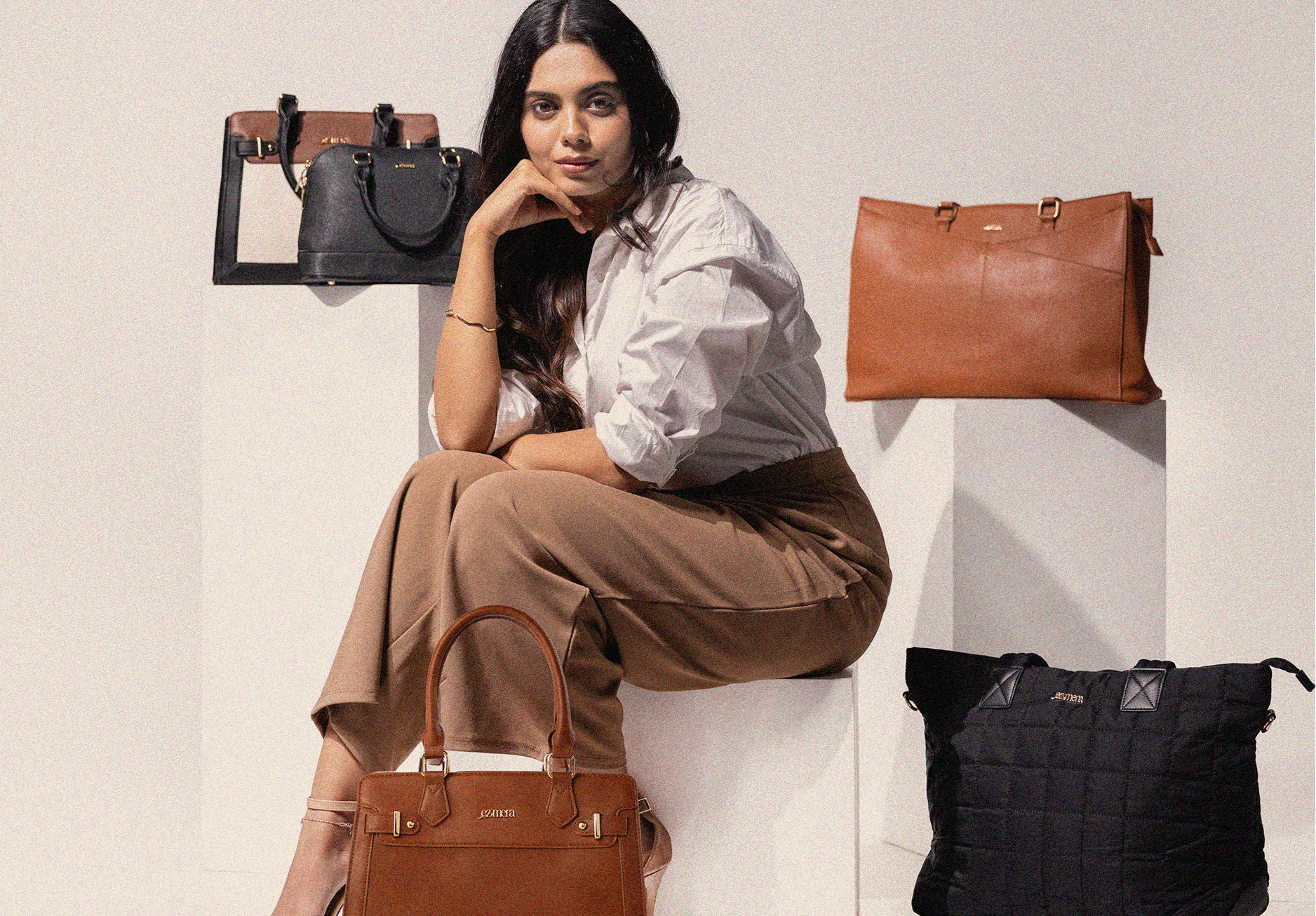Woman sitting with various leather bags displayed around her on a light background